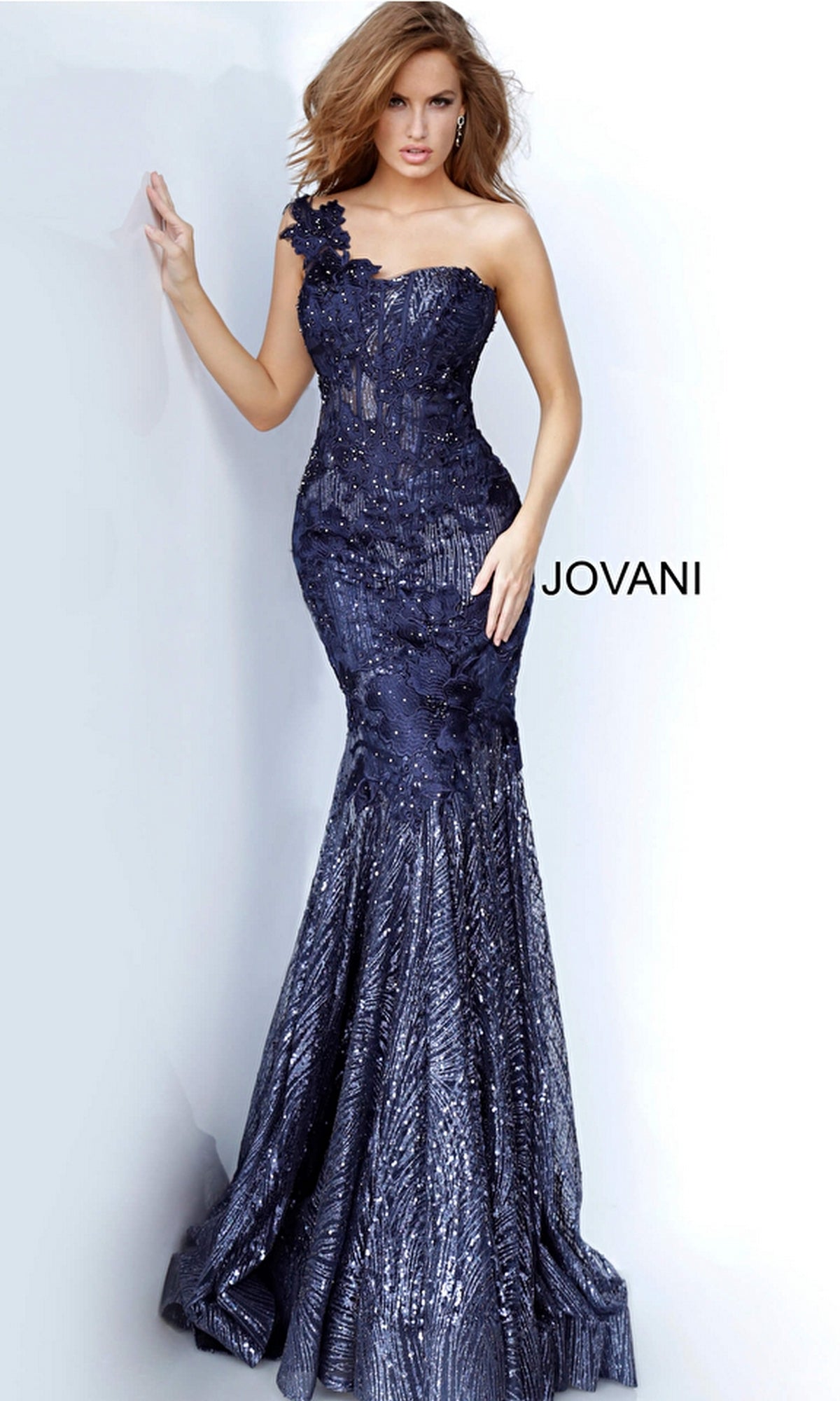 Woman wearing the Jovani One-Shoulder Glitter Long Prom Dress 02445, a dark blue floor-length gown with sequin embellishments and a floral applique on one shoulder.